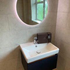 Circular illuminated bathroom mirror above wall hung basin - Thomson Properties