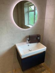 Circular illuminated bathroom mirror above wall hung basin - Thomson Properties